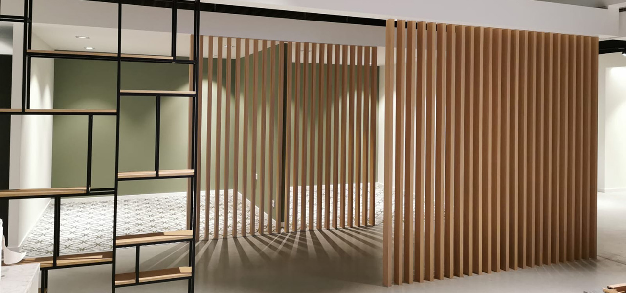 Een moderne ruimte met houten verticale lamellen die dienen als afscheiding, met een groene muur en vloeren met een geometrisch patroon, geflankeerd door een metalen rek met houten planken.