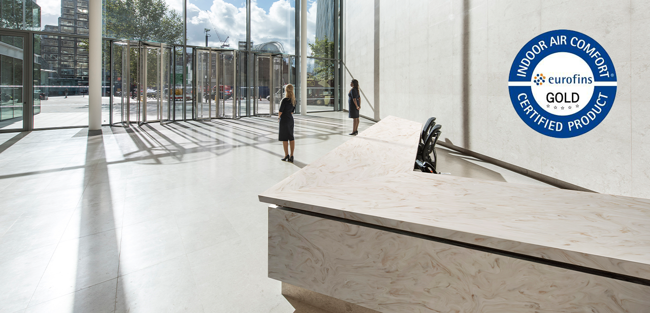Grote receptieruimte met een Corian® Solid Surface balie, Eurofins Indoor Air Comfort Gold-certificaat zichtbaar, onder een helder, hoog plafond met veel natuurlijk lichtinval.