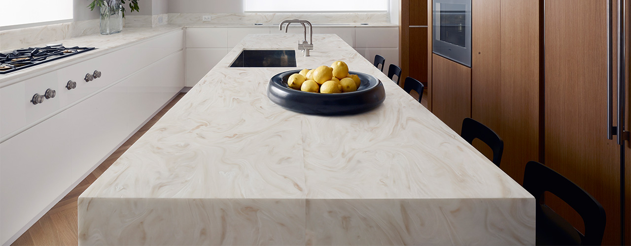 Keukenblad gemaakt van Corian® solid surface materiaal met een marmerachtig patroon, voorzien van geïntegreerde gootsteen en opstelling van stoelen langs het blad.