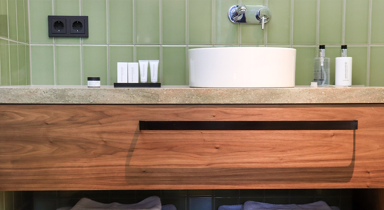 Hotel MAI Amsterdam 1 – Badkamermeubel met houten lade, groen tegelwerk en witte waskom.