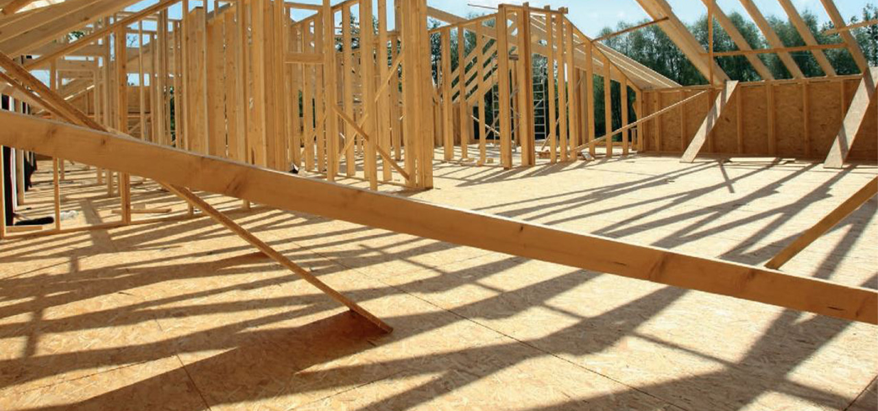 Een houten constructie in aanbouw met OSB-platen op de vloer en een houten skelet voor de muren en het dak, verlicht door zonlicht.