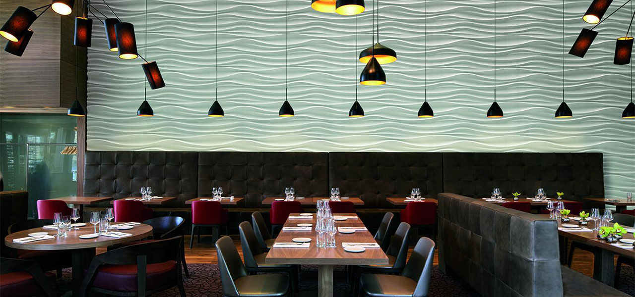 Een stijlvol restaurant met een muur voorzien van golvende witte 3D-panelen, verlicht door moderne, hangende lampen.