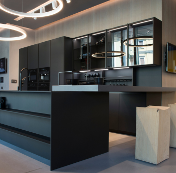 Moderne keuken met een zwart Fenix aanrechtblad en ge&iuml;ntegreerde kookplaat, minimalistisch design met glazen en kookgerei op het aanrecht.