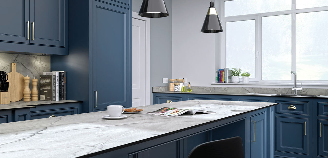 Elegante keuken met diepblauwe kastfronten en een marmeren werkblad. De keuken is ingericht met moderne zwarte hanglampen, een groot raam met uitzicht op een groen landschap en decoratieve accessoires zoals houten snijplanken en boeken. 