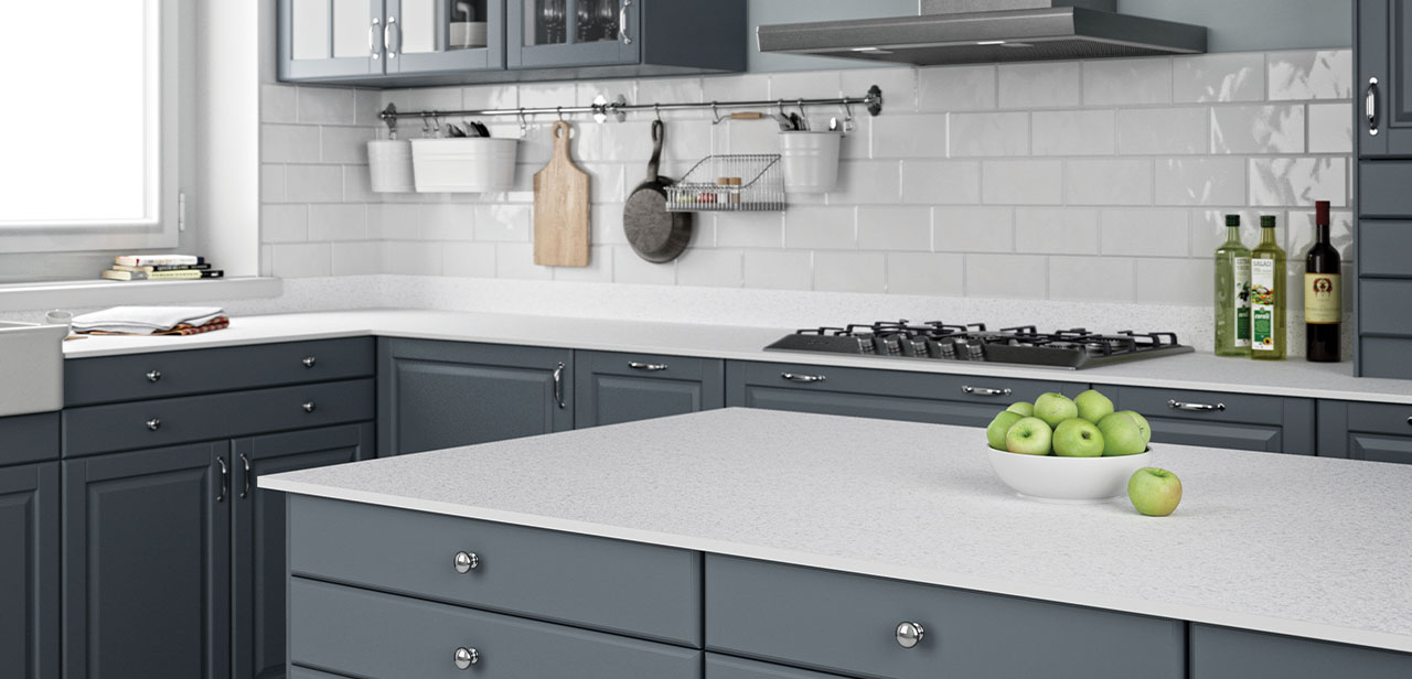 Klassieke keuken met een tijdloos design, voorzien van donkergrijze kastfronten met chromen knoppen, een strak wit werkblad en een witte metrotegel-achterwand. De schaal met groene appels op het eiland vormt een fris contrast.