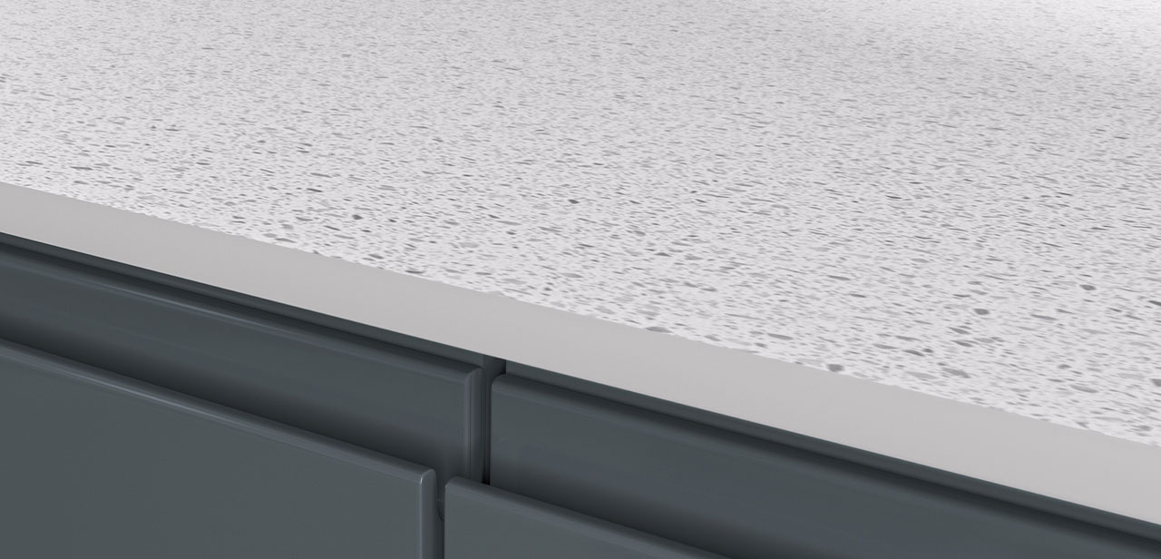 Gedetailleerde close-up van een wit gespikkeld werkblad met een gladde en naadloze afwerking. Het werkblad rust op donkergrijze kastfronten met een minimalistisch ontwerp en afgeronde hoeken.
