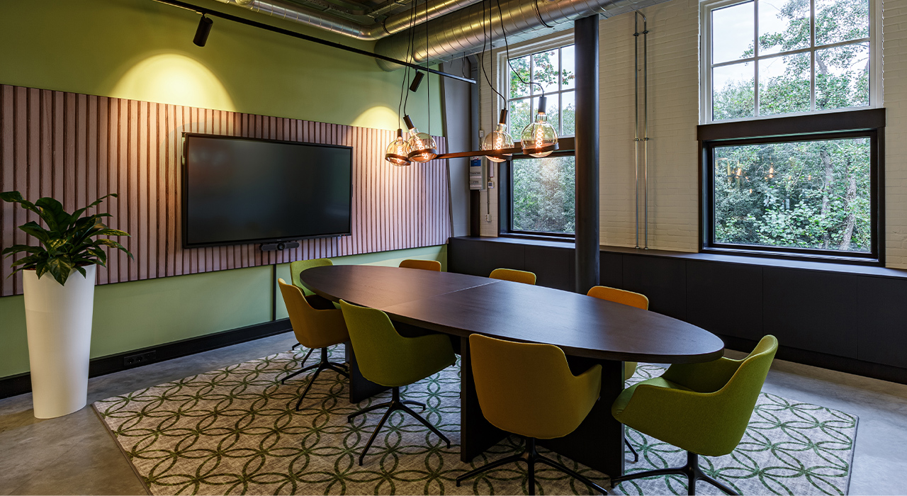 Your Controller Vught 2 – Vergaderruimte met ovale tafel, groene stoelen en grote ramen.