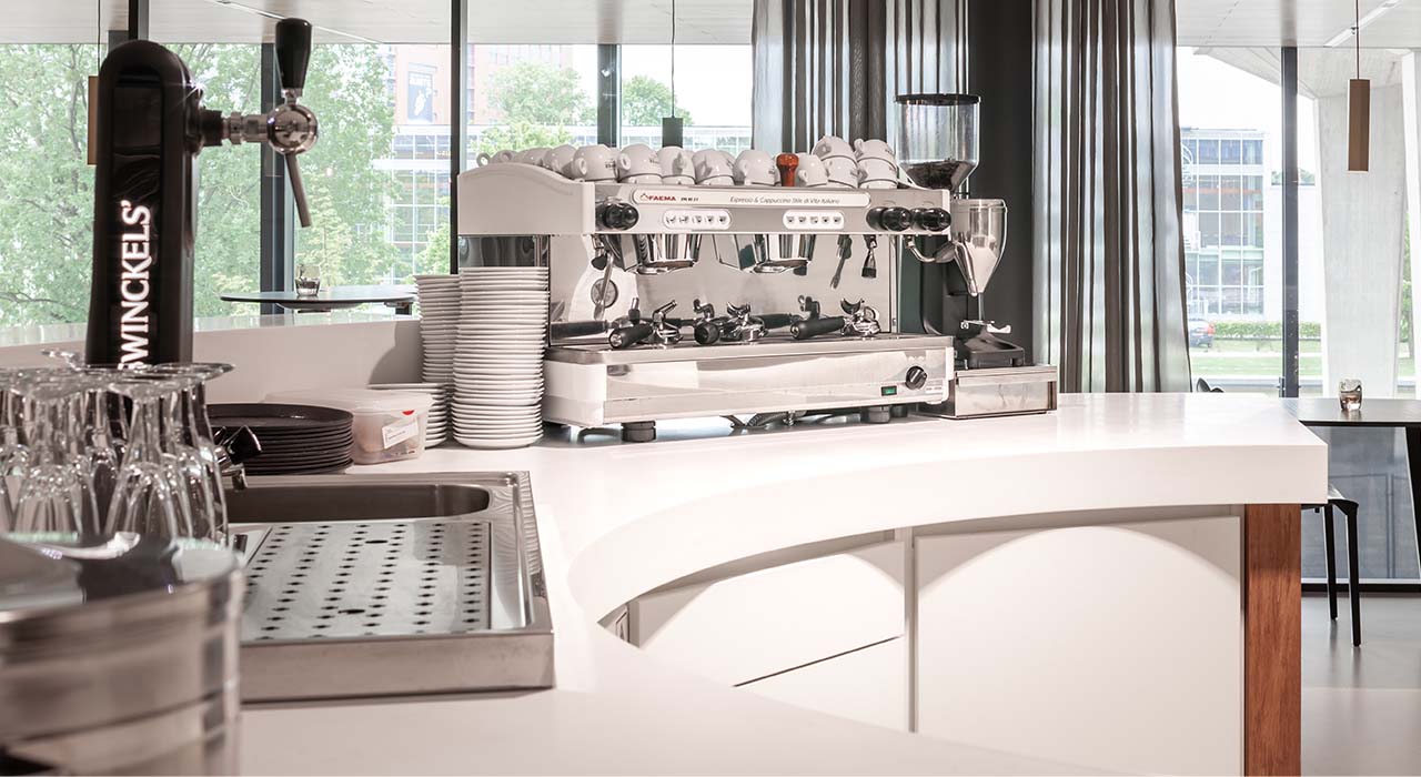 Koffiecorner met professionele espressomachine en glazen achterwand in universiteitsbar aan de Technische Universiteit Eindhoven.