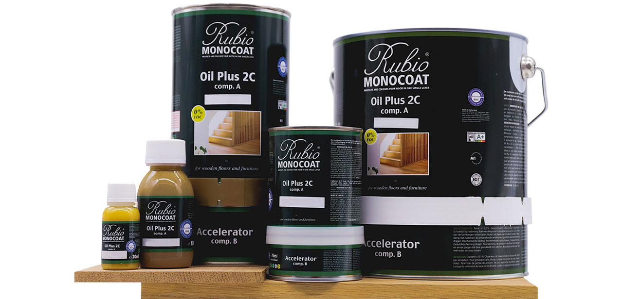 Verschillende blikken en flessen Rubio Monocoat Oil Plus 2C houtolie, in diverse maten, gepresenteerd op een houten oppervlak.