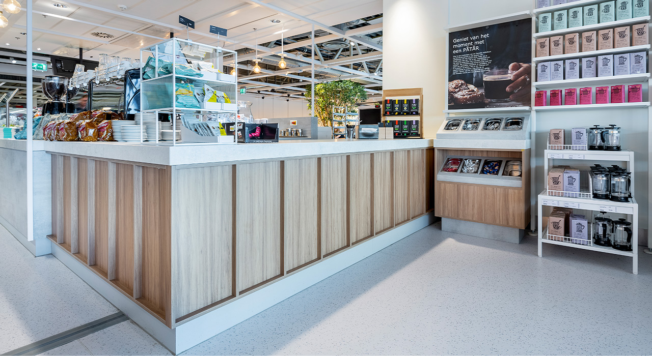 Moderne koffiebar met houten front en wit werkblad, voorzien van een espressomachine, snacks en een display met koffieproducten.