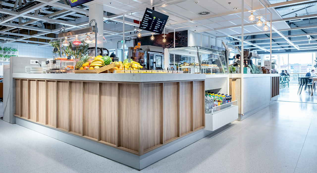 Juicebar met vers fruit en een fris, modern design, met een digitaal menu erboven en een lichte houtafwerking.
